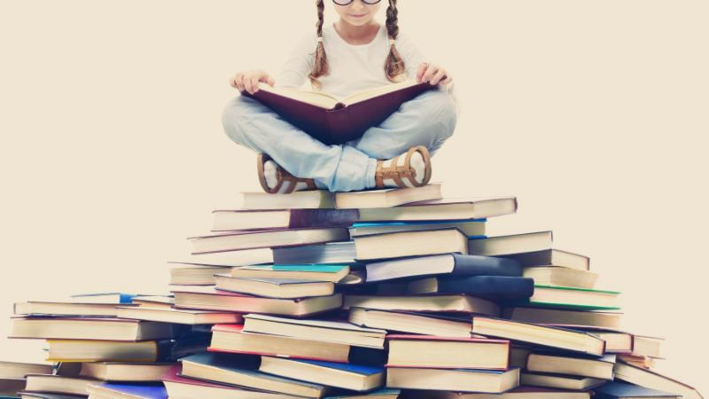 Girl reading on top of pile of books